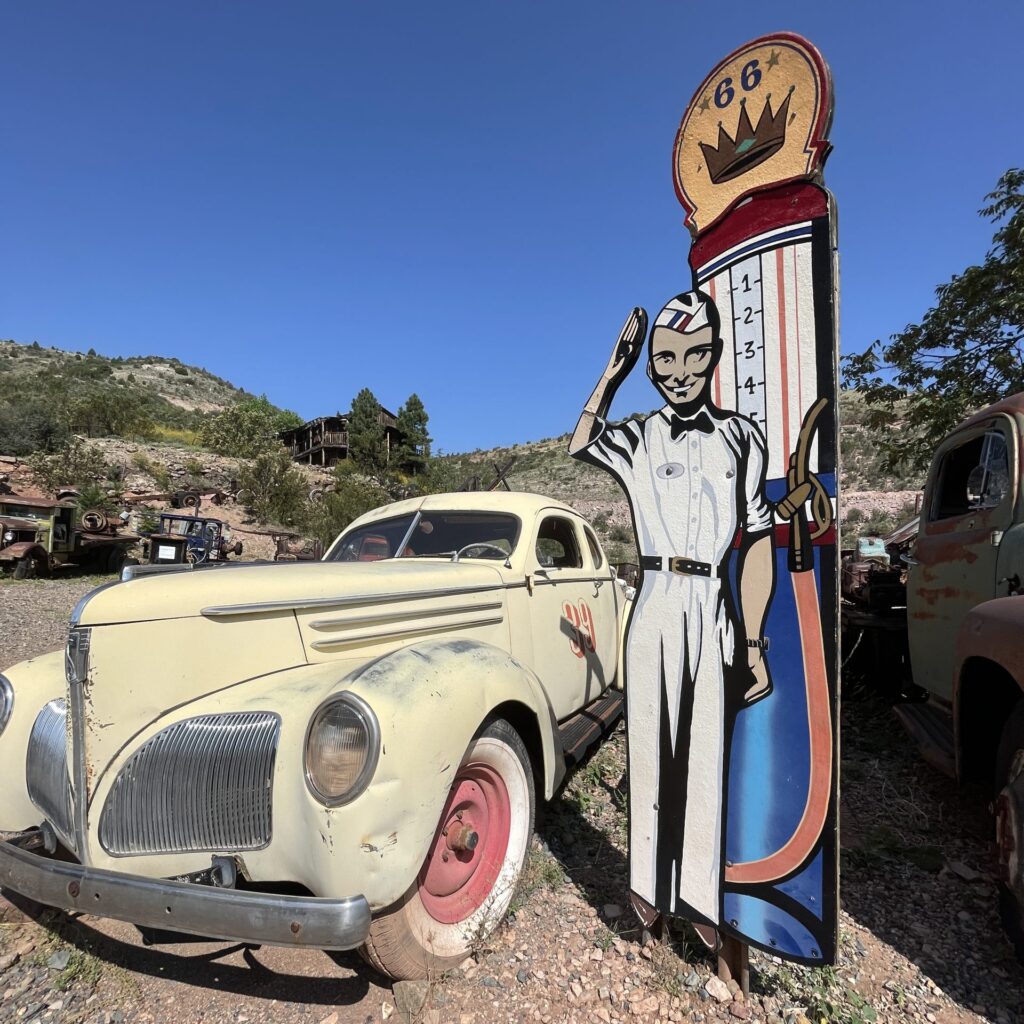 a cardboard cutout of a 50's style gas station attendant next to a classic car and gas pump